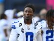 Cowboys linebacker DeMarvion Overshown, a towel draped around his neck, walks along the sideline in his white No. 0 jersey.