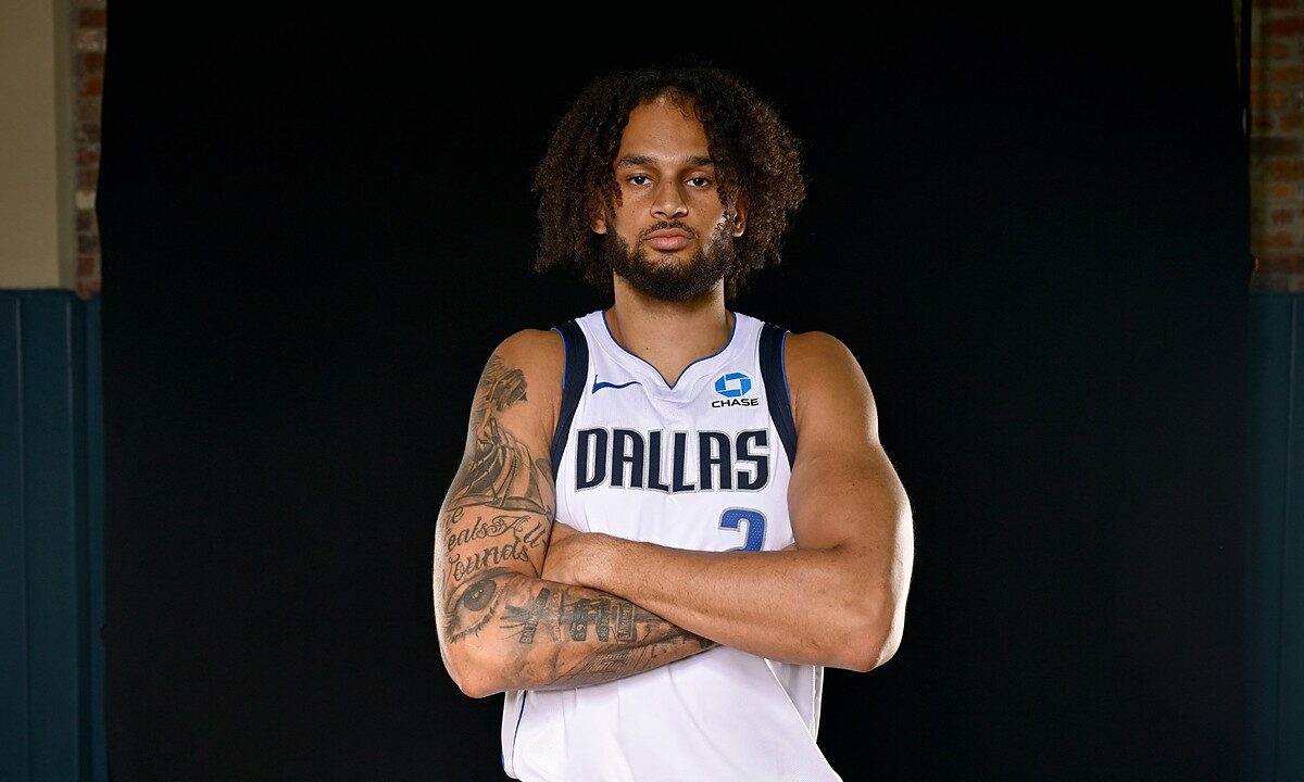 Dallas Mavericks center Dereck Lively II stands with his tattooed arms crossed in a white Dallas No. 2 jersey.