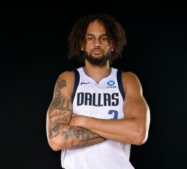 Dallas Mavericks center Dereck Lively II stands with his tattooed arms crossed in a white Dallas No. 2 jersey.
