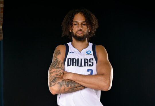 Dallas Mavericks center Dereck Lively II stands with his tattooed arms crossed in a white Dallas No. 2 jersey.