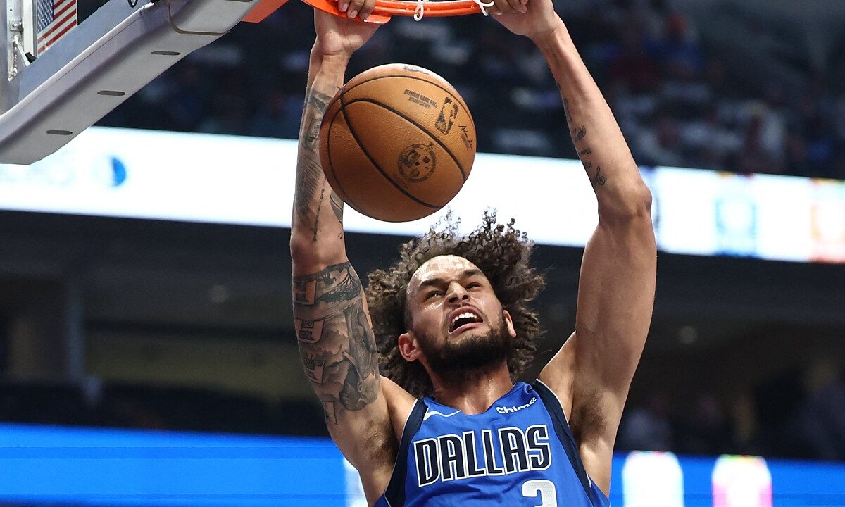 Dallas Mavericks center Dereck Lively II hangs on the rim with both hands after a two-handed dunk.