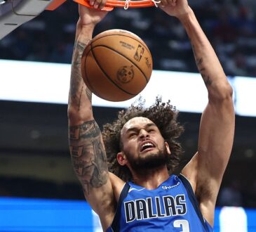 Dallas Mavericks center Dereck Lively II hangs on the rim with both hands after a two-handed dunk.