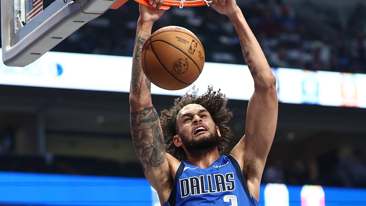 Dallas Mavericks center Dereck Lively II hangs on the rim with both hands after a two-handed dunk.
