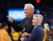 Former Dallas Mavericks coach Donald Nelson smiles and points while holding a glass award on the court.