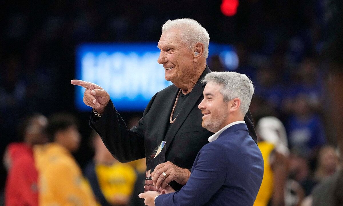 Former Dallas Mavericks coach Donald Nelson smiles and points while holding a glass award on the court.
