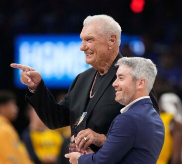 Former Dallas Mavericks coach Donald Nelson smiles and points while holding a glass award on the court.