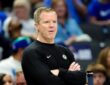 Dallas Mavericks head coach Dusty May stands with his arms crossed on the sideline as fans watch behind him.