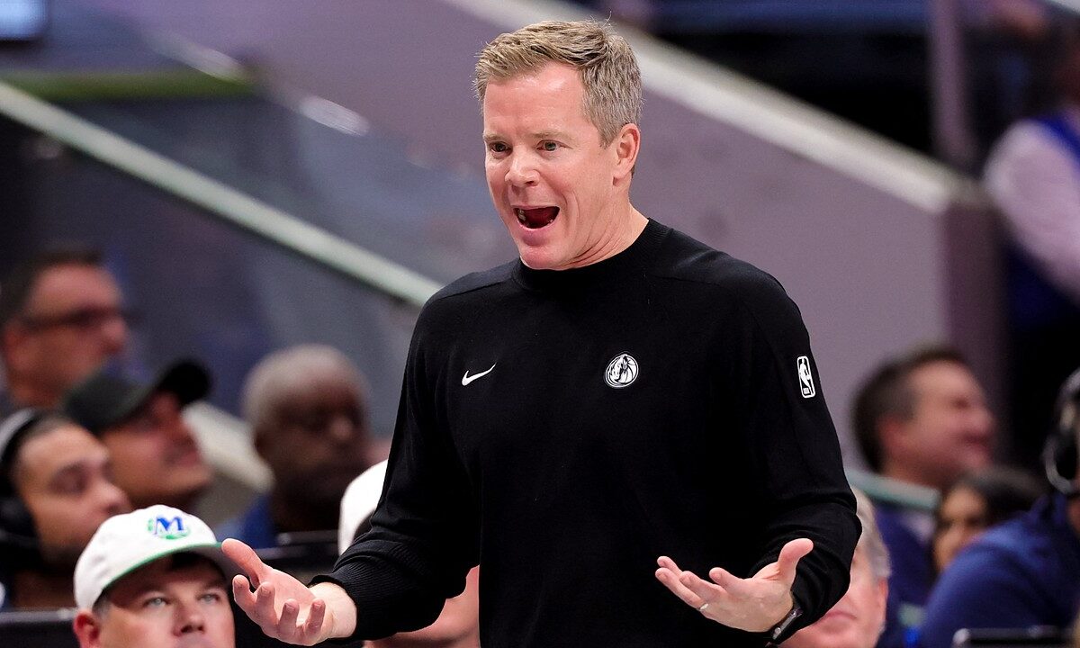 Dallas Mavericks head coach Dusty May reacts on the sideline with his mouth open and both palms turned up as fans look on.