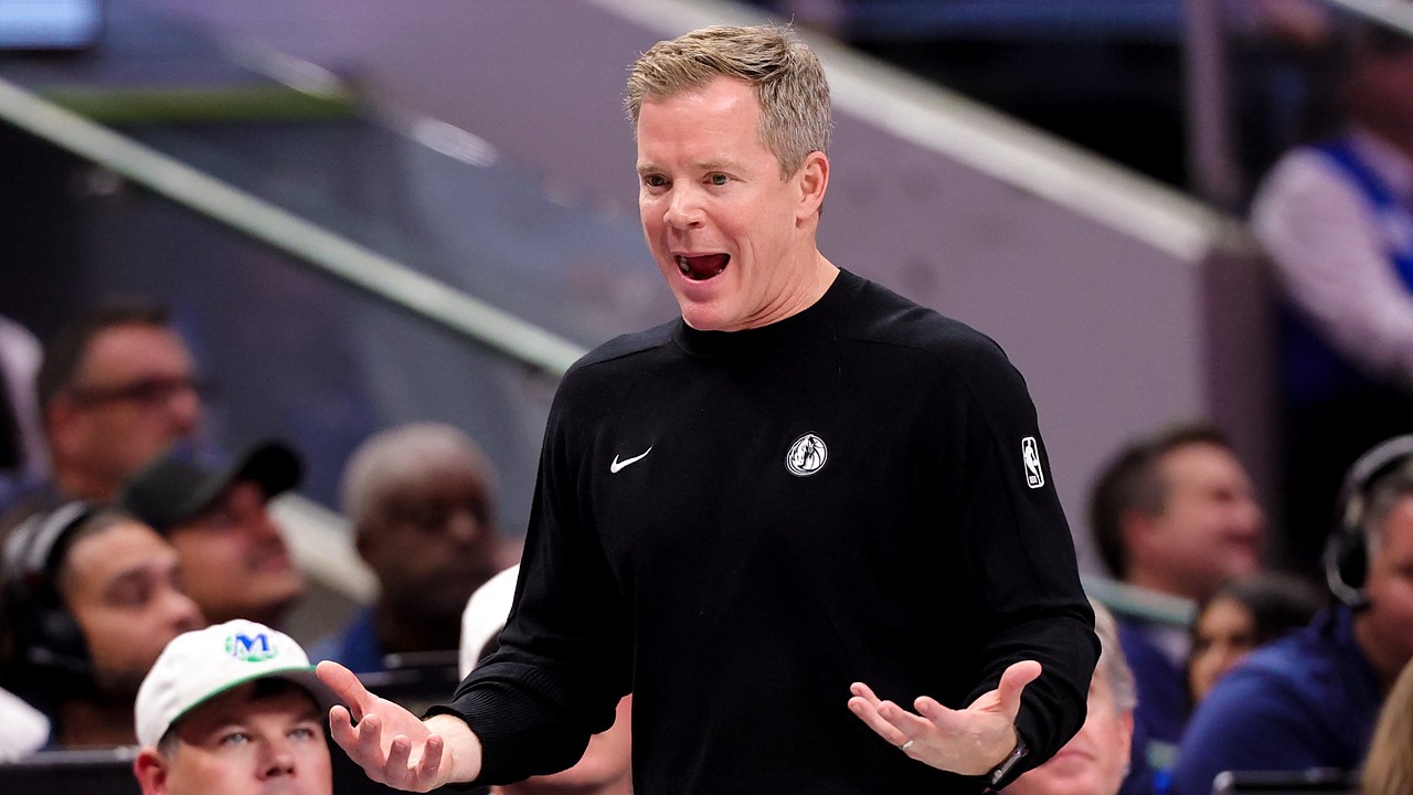 Dallas Mavericks head coach Dusty May reacts on the sideline with his mouth open and both palms turned up as fans look on.