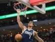 Mavericks center Dwight Powell hangs on the rim after a one-handed dunk as the ball drops through the net.