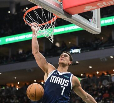 Mavericks center Dwight Powell hangs on the rim after a one-handed dunk as the ball drops through the net.