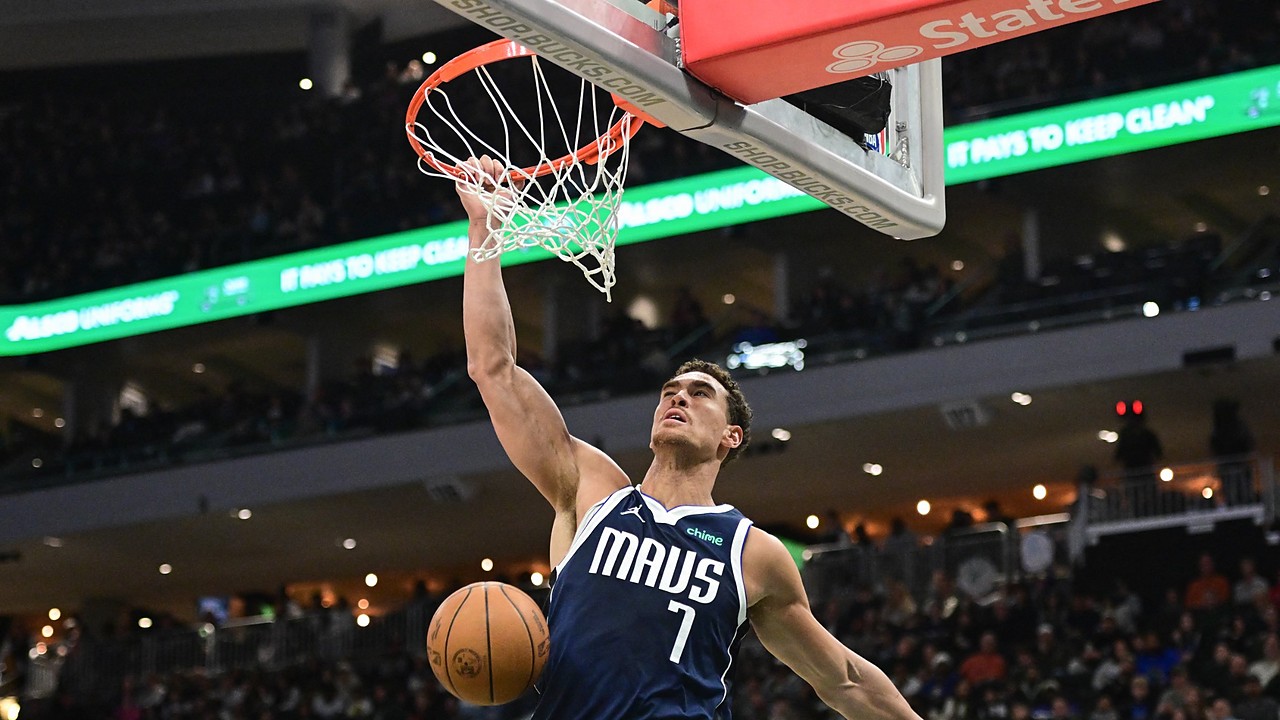 Mavericks center Dwight Powell hangs on the rim after a one-handed dunk as the ball drops through the net.
