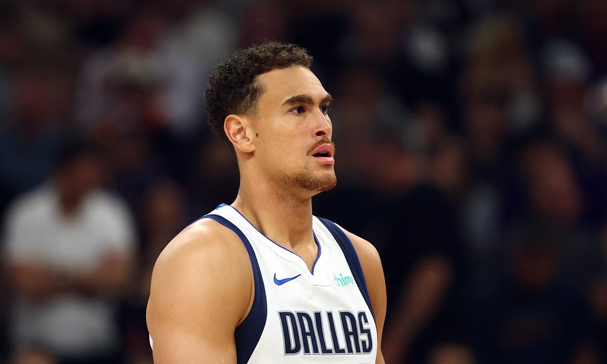 Dallas Mavericks forward Dwight Powell stands on the court looking toward the action in a white Dallas jersey.