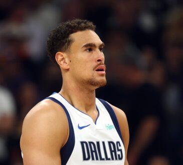 Dallas Mavericks forward Dwight Powell stands on the court looking toward the action in a white Dallas jersey.