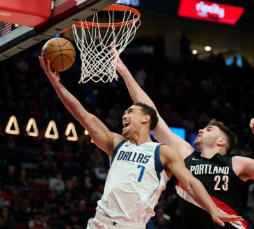 Dallas Mavericks forward Dwight Powell lays the ball up at the rim as Portland Trail Blazers center Donovan Clingan reaches to contest.