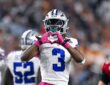 Dallas Cowboys wide receiver George Pickens makes a heart shape with his pink gloves in front of his face mask.