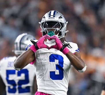 Dallas Cowboys wide receiver George Pickens makes a heart shape with his pink gloves in front of his face mask.