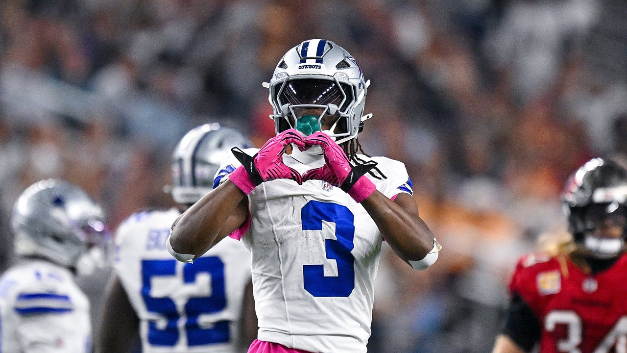 Dallas Cowboys wide receiver George Pickens makes a heart shape with his pink gloves in front of his face mask.