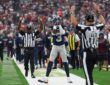 Cowboys wide receiver George Pickens covers his face mask with both hands as two officials raise their arms on the sideline.