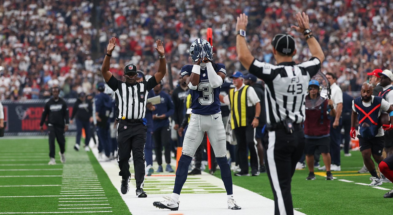 Cowboys wide receiver George Pickens covers his face mask with both hands as two officials raise their arms on the sideline.