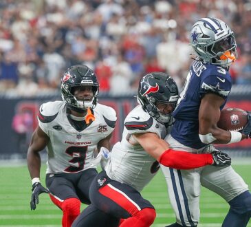 Cowboys wide receiver George Pickens clutches the ball as a Texans defender wraps him up from behind.