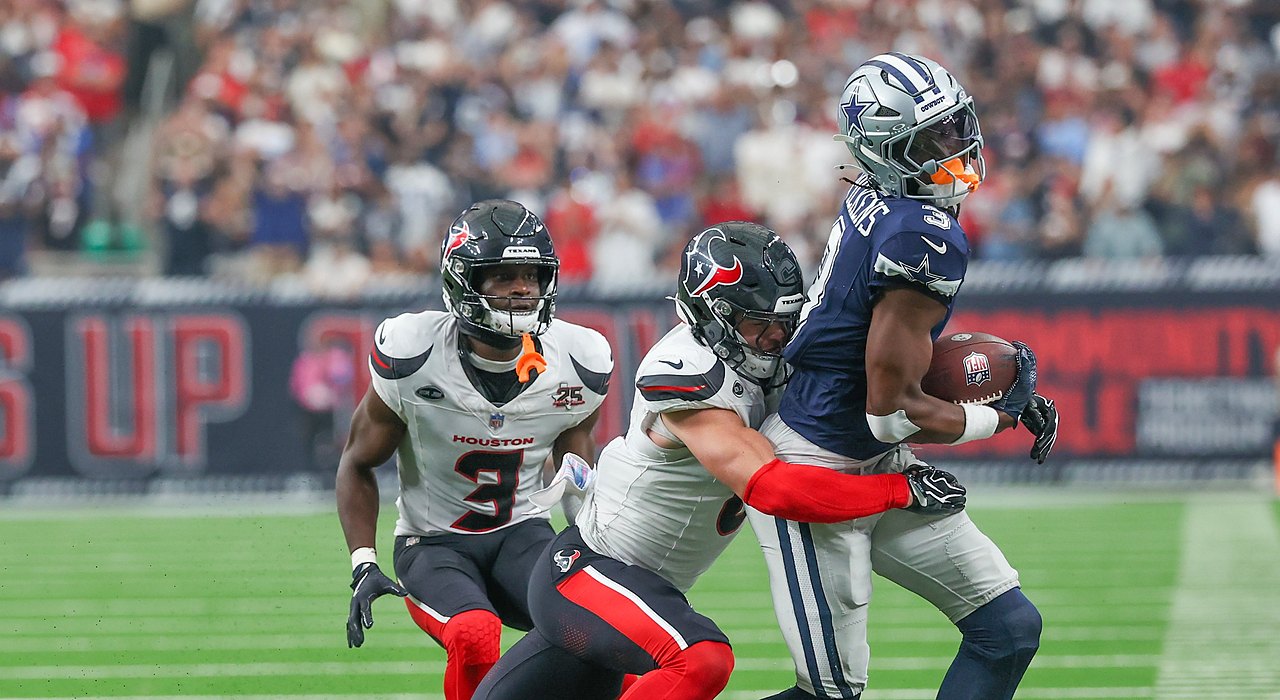 Cowboys wide receiver George Pickens clutches the ball as a Texans defender wraps him up from behind.
