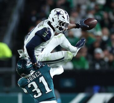Dallas Cowboys wide receiver George Pickens hurdles over an Eagles cornerback with the ball stretched out in one hand.