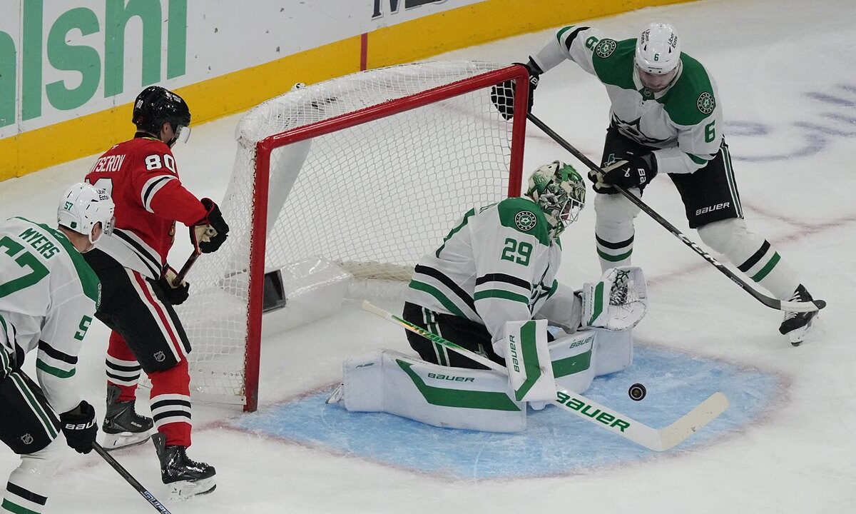 Dallas Stars goaltender Jake Oettinger drops to his knees to block a puck in the crease as Blackhawks and Stars players close in.