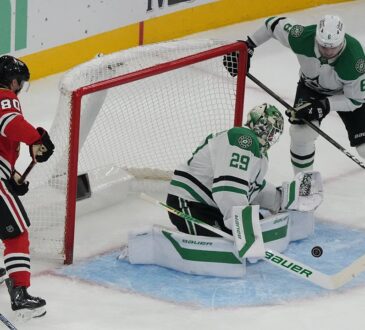 Dallas Stars goaltender Jake Oettinger drops to his knees to block a puck in the crease as Blackhawks and Stars players close in.
