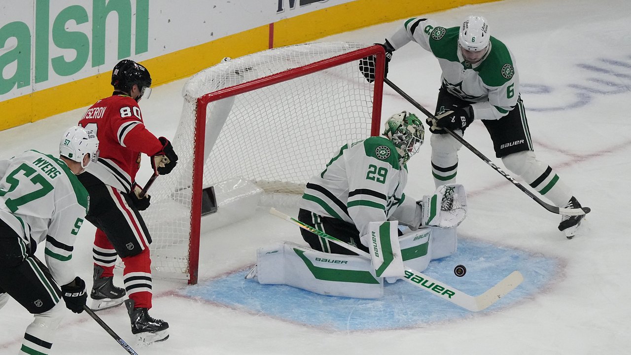 Dallas Stars goaltender Jake Oettinger drops to his knees to block a puck in the crease as Blackhawks and Stars players close in.