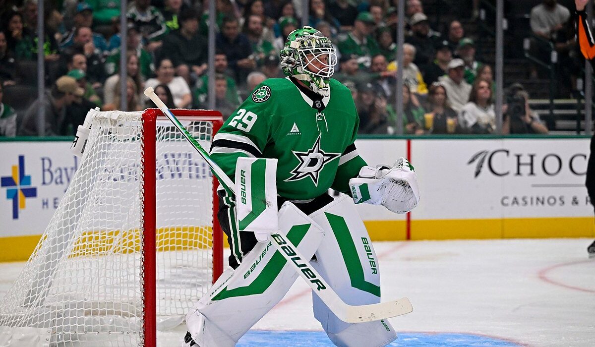Stars goaltender Jake Oettinger crouches in his crease beside the net, watching the play with his glove raised.