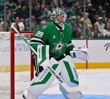 Stars goaltender Jake Oettinger crouches in his crease beside the net, watching the play with his glove raised.