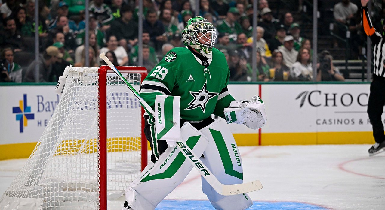 Stars goaltender Jake Oettinger crouches in his crease beside the net, watching the play with his glove raised.