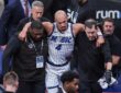Orlando Magic guard Jalen Suggs is helped off the court by two team staff members, with his arms over their shoulders.