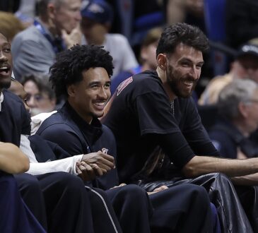 Oklahoma City Thunder players Jalen Williams, Jared McCain, and Chet Holmgren smile while watching from the bench in street clothes.