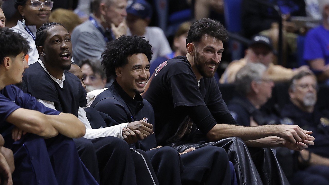 Oklahoma City Thunder players Jalen Williams, Jared McCain, and Chet Holmgren smile while watching from the bench in street clothes.