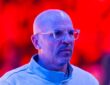 Then-Dallas Mavericks head coach Jason Kidd looks on in clear glasses and a light blue quarter-zip under red arena lights.