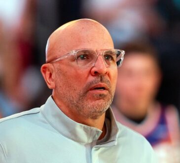 Then-Mavericks head coach Jason Kidd, wearing clear-framed glasses, looks on from the sideline with fans behind him.