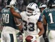 Dallas Cowboys running back Javonte Williams raises his hand and holds the football after scoring, with Philadelphia Eagles players around him.
