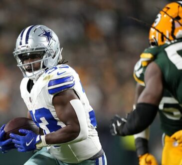 Dallas Cowboys running back Javonte Williams cradles the ball with both hands as a Green Bay Packers defender closes in.