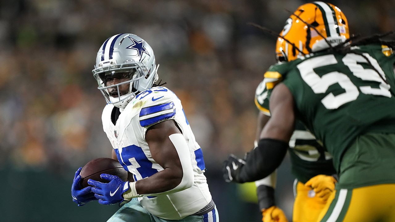 Dallas Cowboys running back Javonte Williams cradles the ball with both hands as a Green Bay Packers defender closes in.