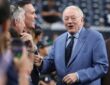 Cowboys owner Jerry Jones smiles and offers a fist bump to fans along the sideline in a blue pinstripe suit.