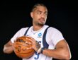Dallas Mavericks guard Jett Howard holds a basketball at his chest and glances to his left against a black backdrop.