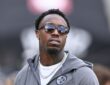 Cornerback Joey Porter Jr., wearing glasses with a black hood pulled over his head, looks on from the field.