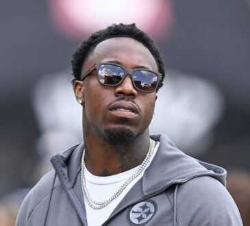Cornerback Joey Porter Jr., wearing glasses with a black hood pulled over his head, looks on from the field.