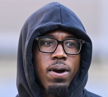 Cornerback Joey Porter Jr., wearing glasses with a black hood pulled over his head, looks on from the field.