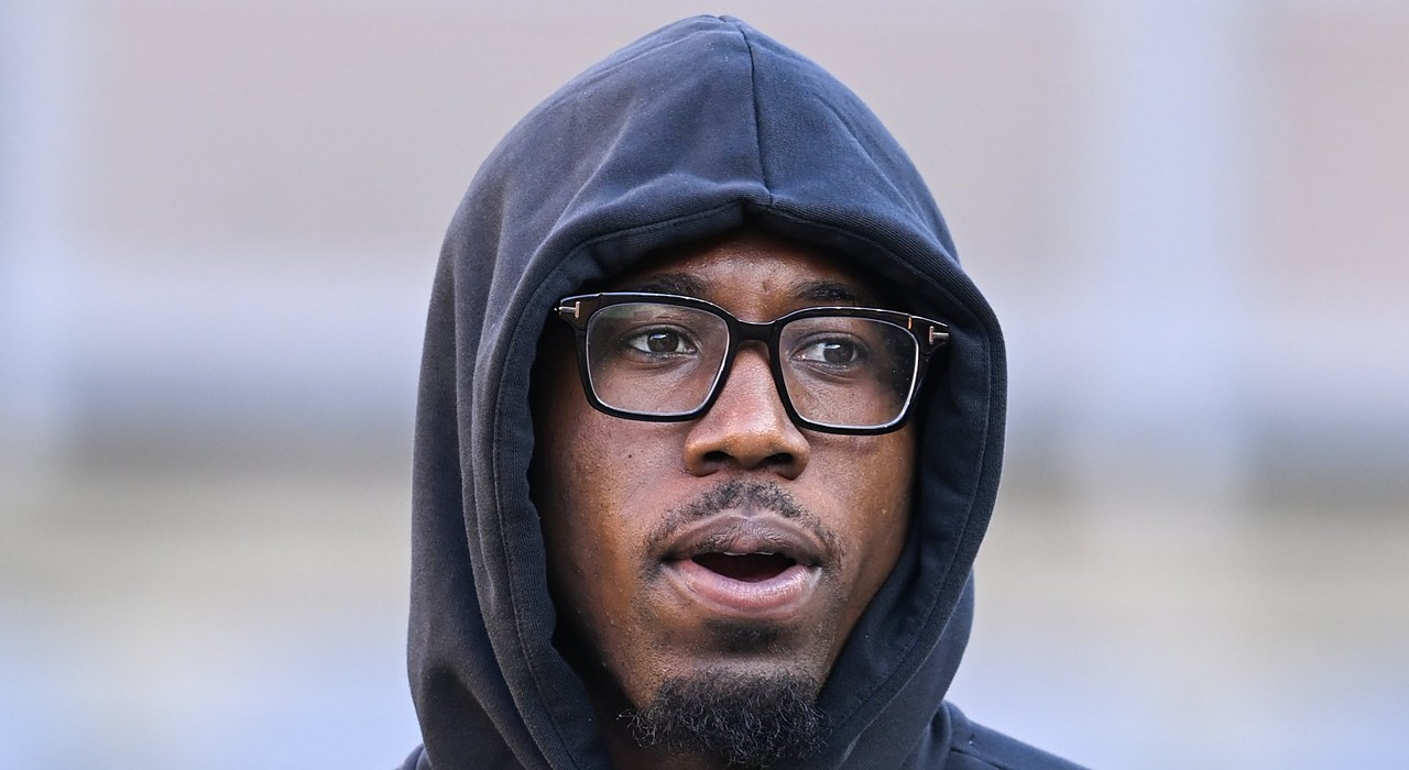 Cornerback Joey Porter Jr., wearing glasses with a black hood pulled over his head, looks on from the field.