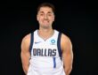 Dallas Mavericks guard John Poulakidas smiles with his hands behind his back in a white Dallas No. 1 jersey.