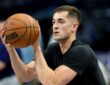 Dallas Mavericks guard John Poulakidas, in a black T-shirt, holds a basketball in shooting position during warmups.