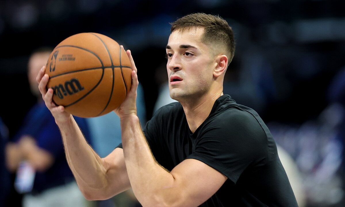 Dallas Mavericks guard John Poulakidas, in a black T-shirt, holds a basketball in shooting position during warmups.